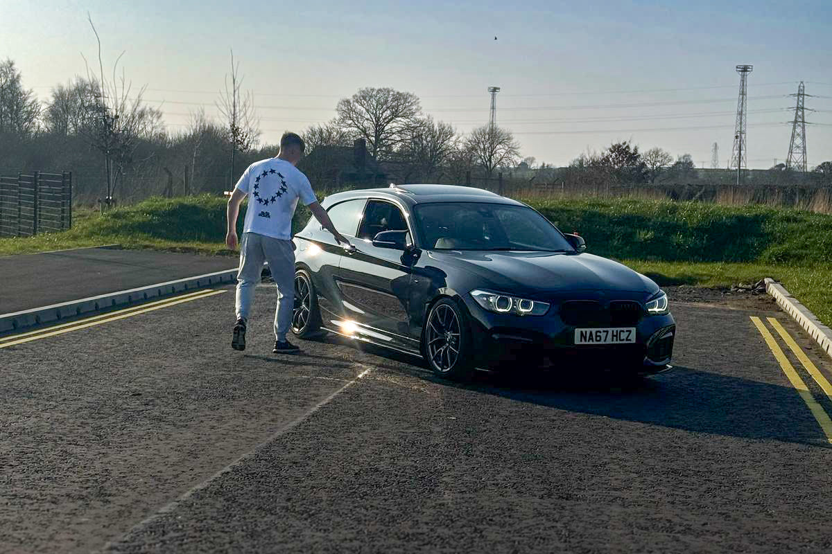 Man applying car detailing product to black car on sunny outdoor road
