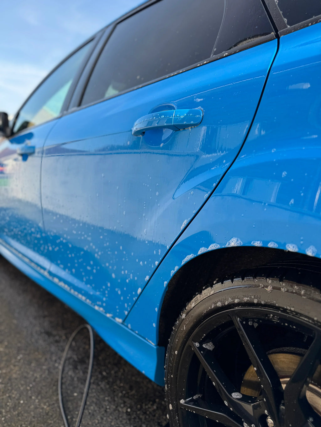 Blue car with soapy water on door and wheel during exterior car wash