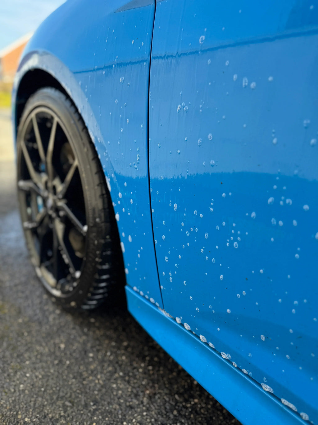 Close-up of blue car with water beading on paint, showcasing car detailing and protective finish