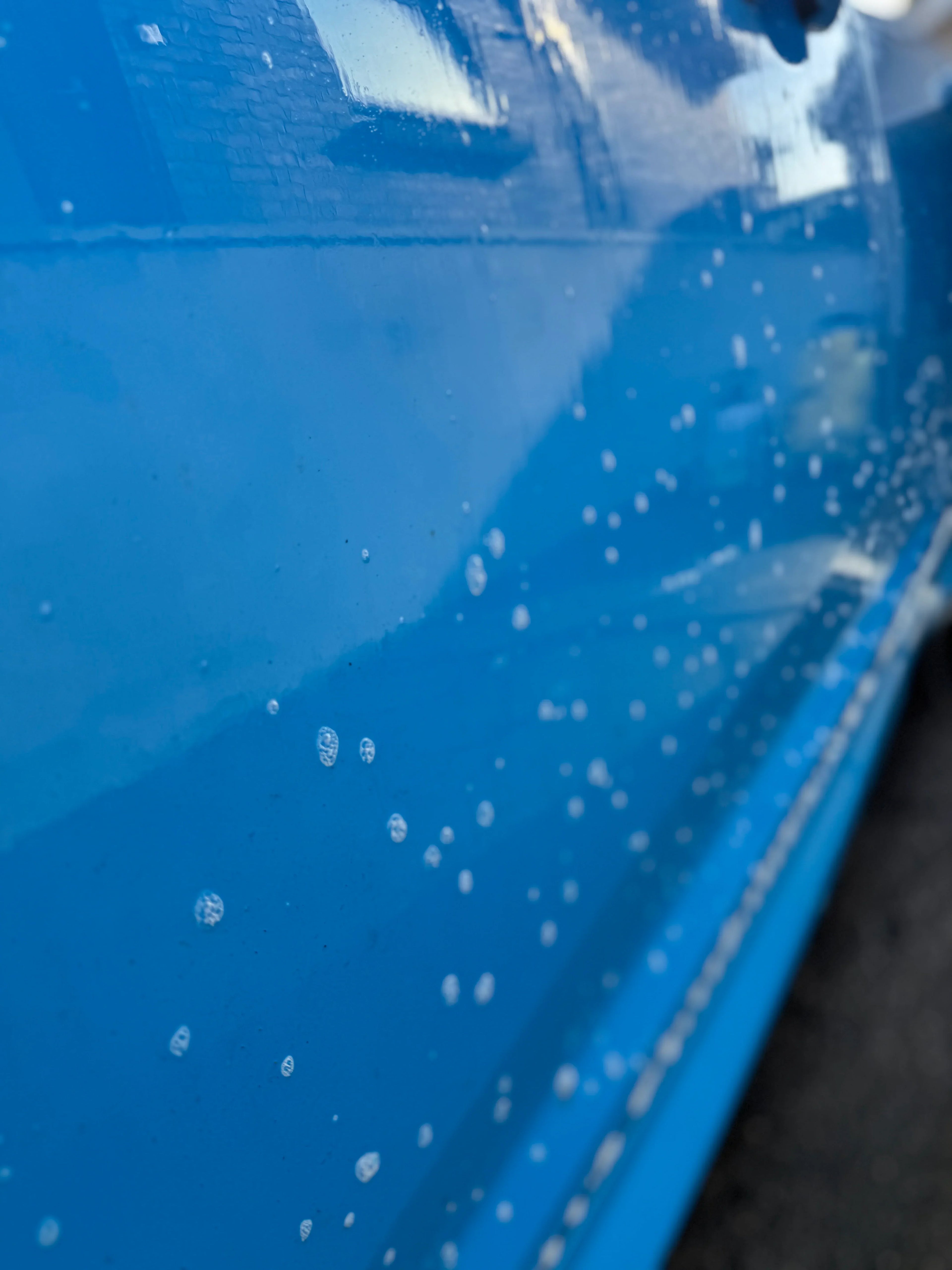 Close-up of blue car door with water spots, showcasing paint finish after car wash.