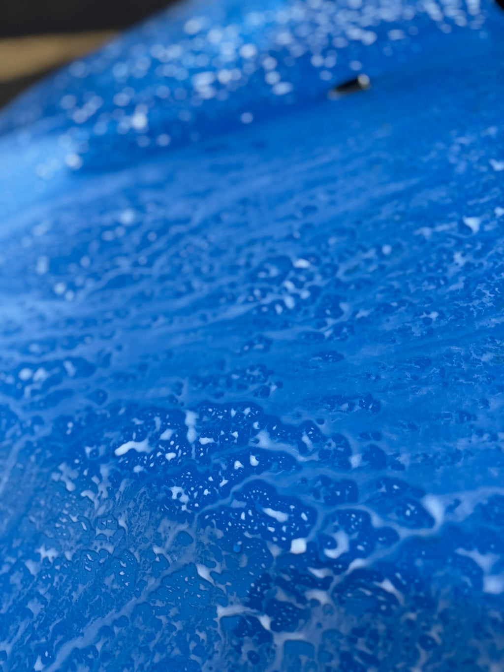 Blue car hood covered in car shampoo suds during automotive detailing wash