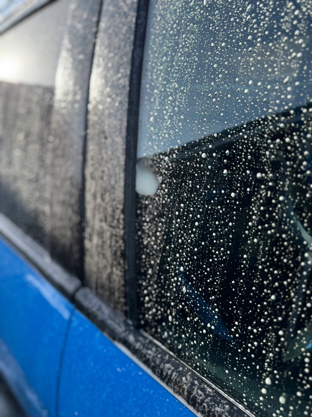 Blue car door and window covered in water beading from car detailing wash