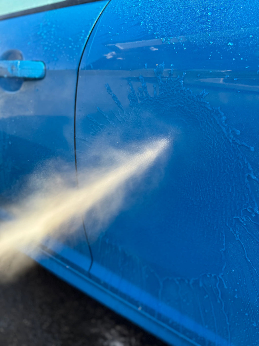 Pressure washing blue car door for car detailing and deep cleaning