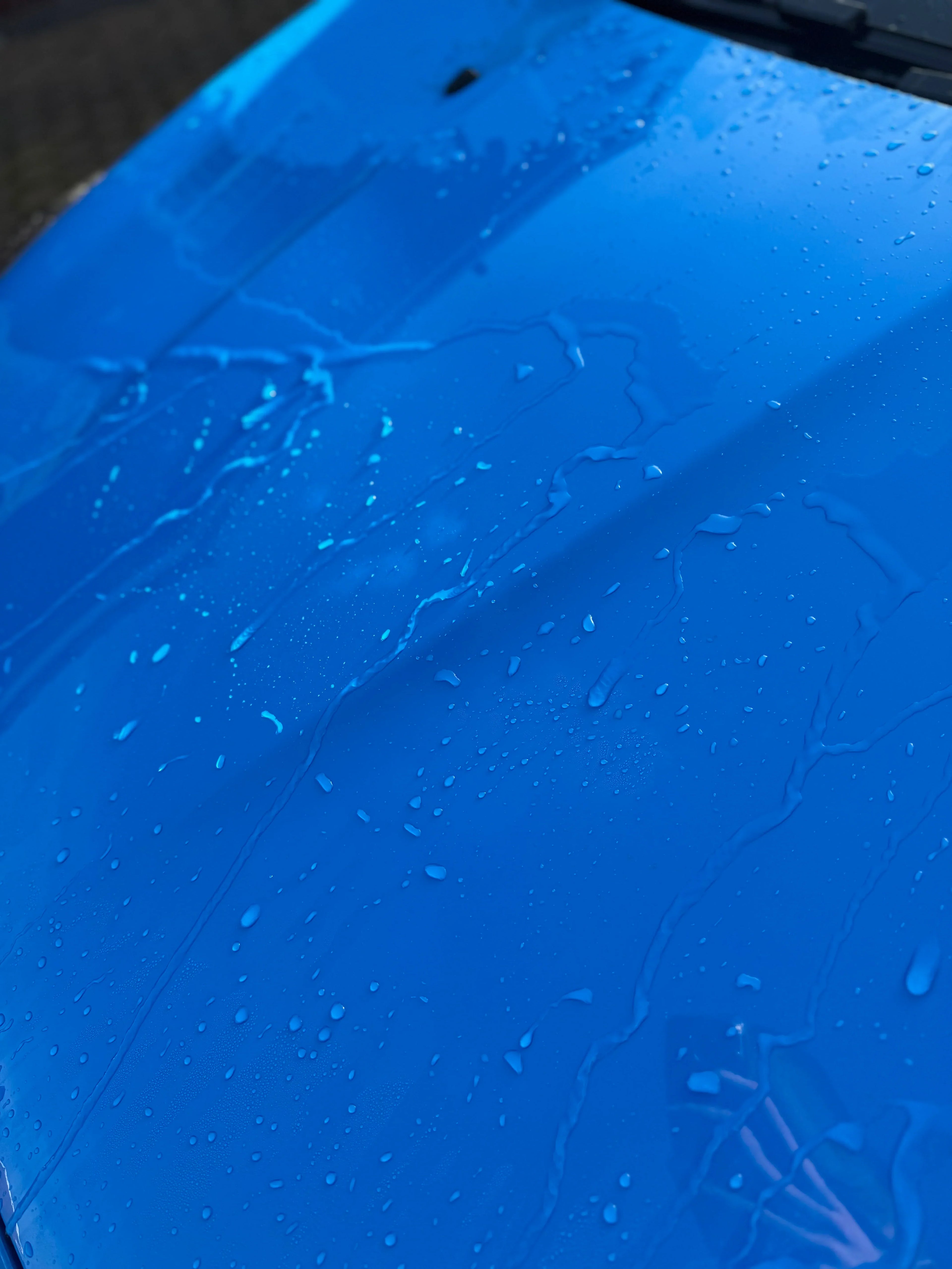 Water beading on a clean blue car hood after using car detailing products