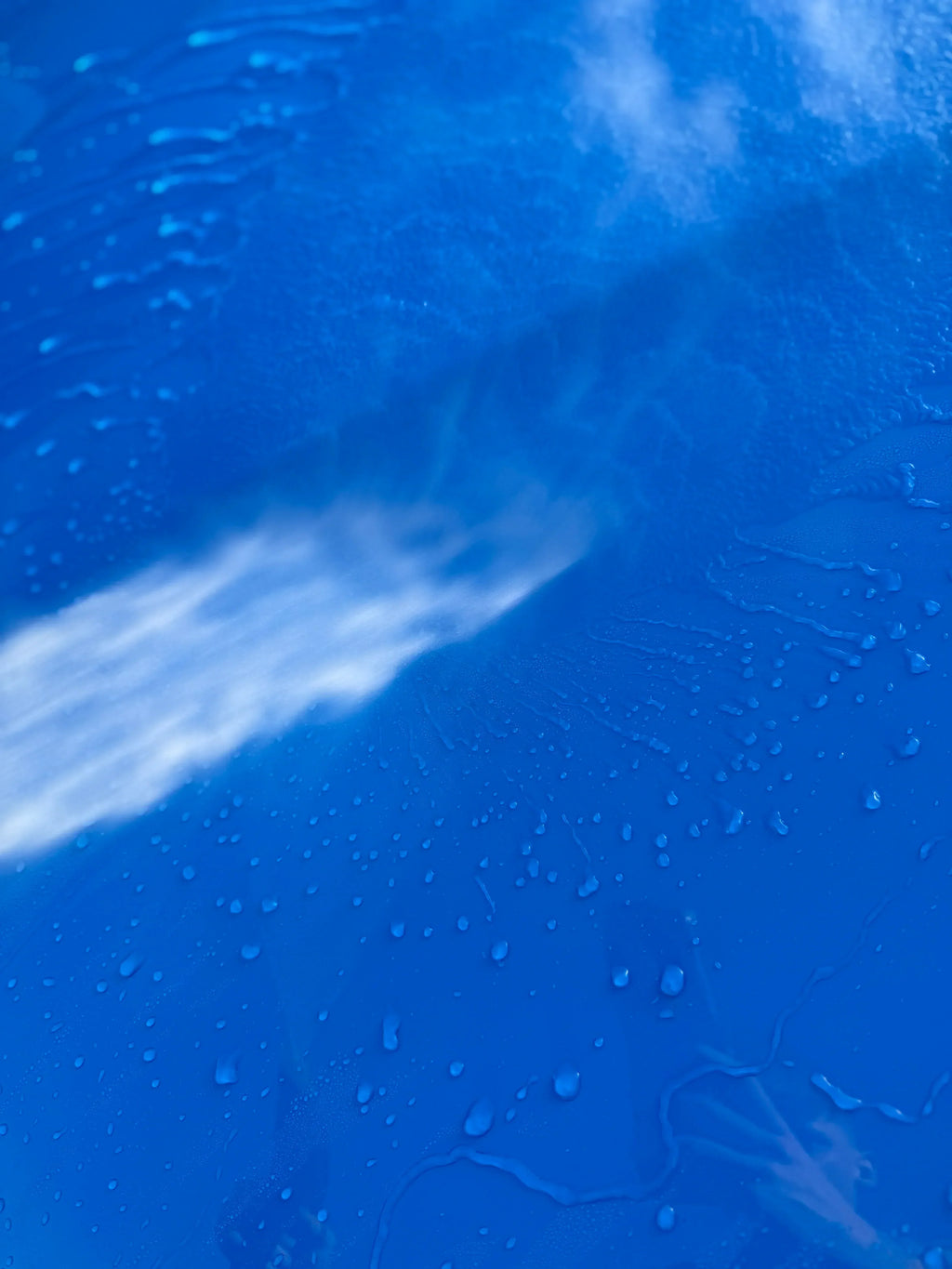 Close-up of water and foam sprayed on a blue car surface during car detailing wash