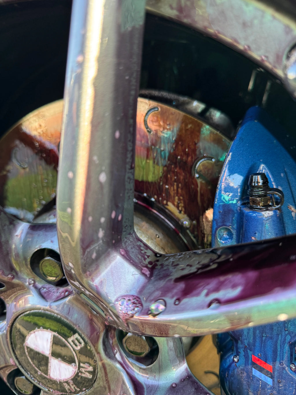 Close-up of a BMW alloy wheel and blue brake caliper with wheel cleaner removing brake dust